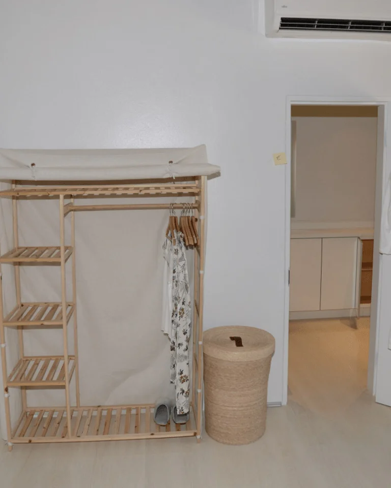 A wooden clothing rack with shelves and a small selection of hanging clothes in a bedroom