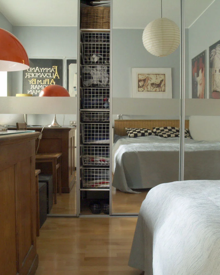 Mirrored sliding wardrobe doors in a bedroom reflecting the bed and storage baskets