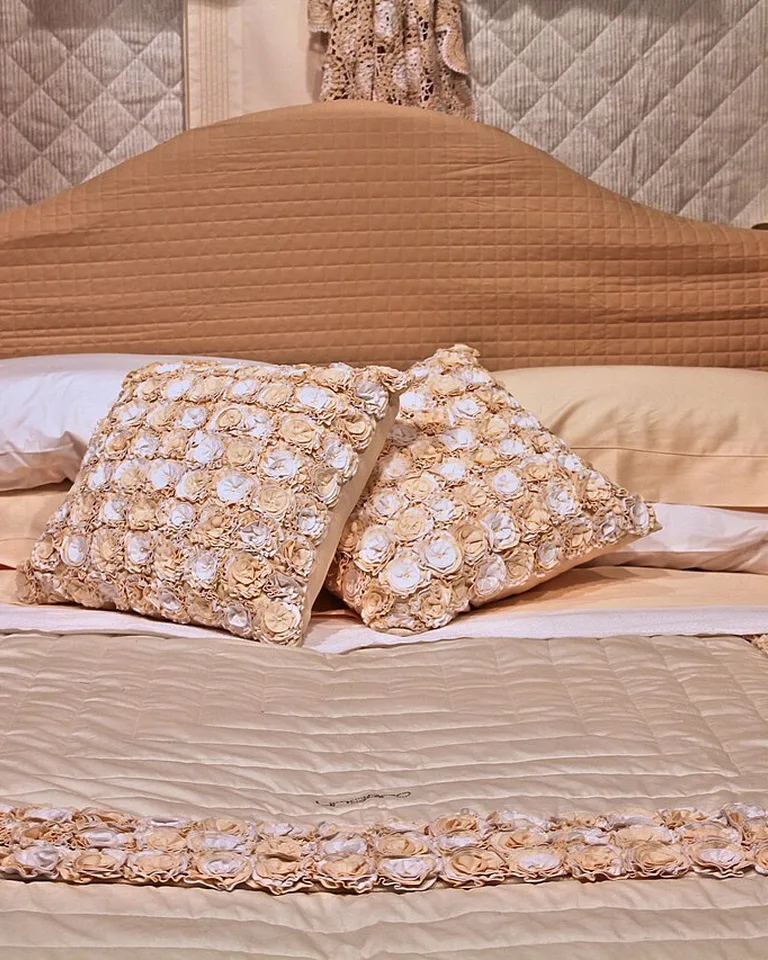 Close-up of a made bed with a quilted beige headboard and textured cream throw pillows