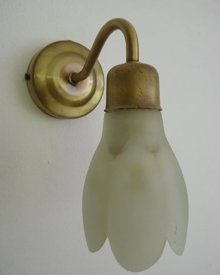 Aged brass wall lamp glowing against an olive green bedroom wall