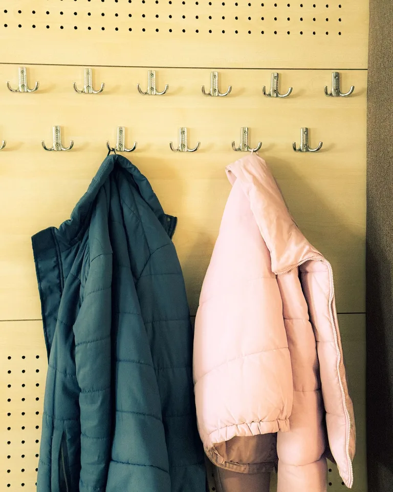 Jackets hanging on hooks of a pegboard-style entryway wall panel