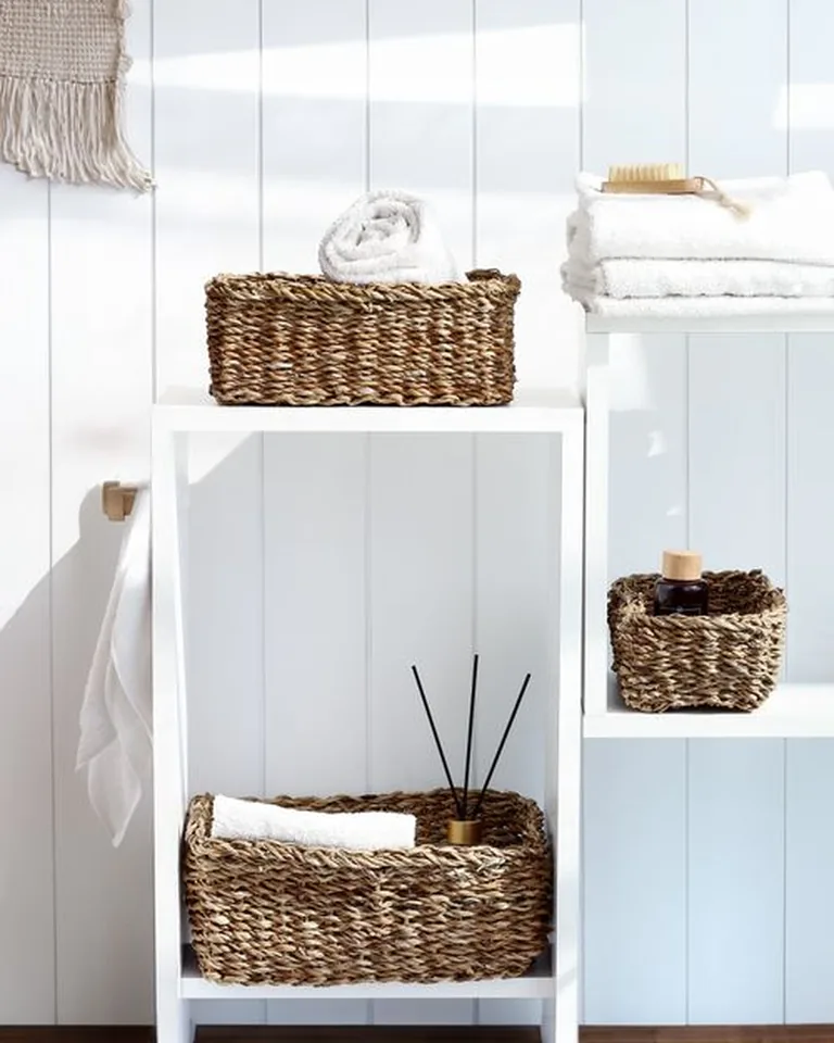 Rental bathroom storage styled with woven baskets, rolled towels, and a freestanding shelf unit