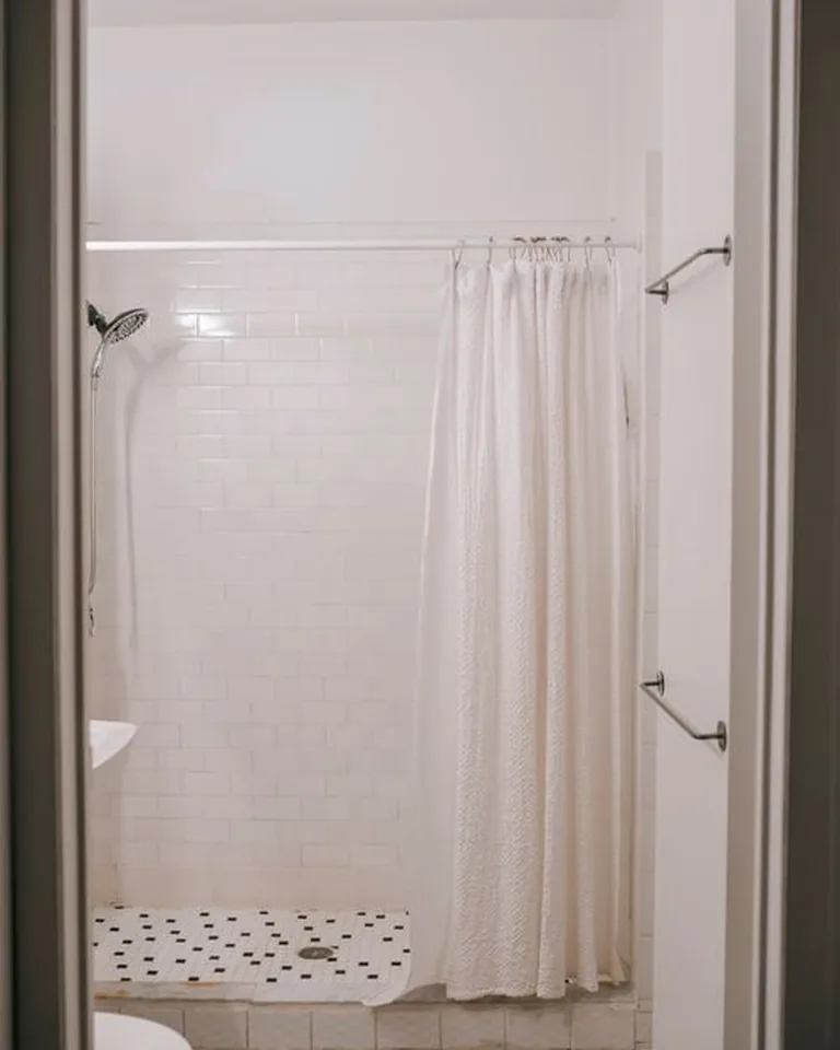Rental bathroom shower with a layered look: linen-look outer curtain over a plain waterproof liner on tension rods