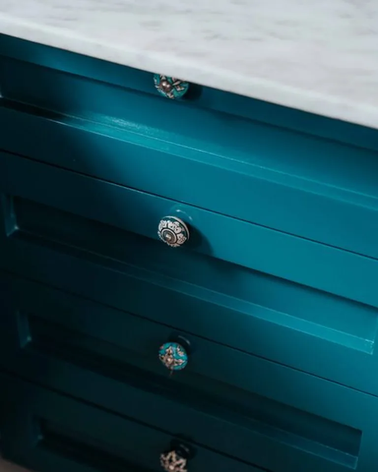 Decorative cabinet knobs on a teal bathroom vanity with a marble countertop