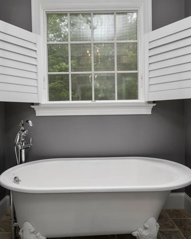 Bathroom window with white privacy shutters above a freestanding tub