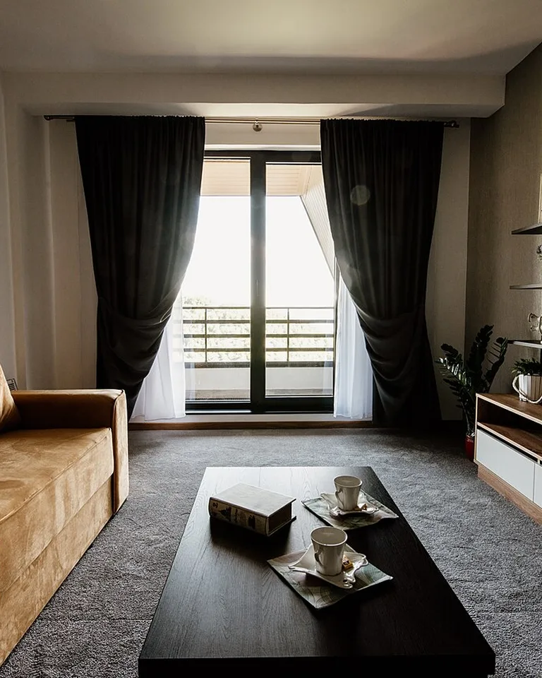 Modern living room with dark curtains, a warm tan sofa, and a styled coffee table