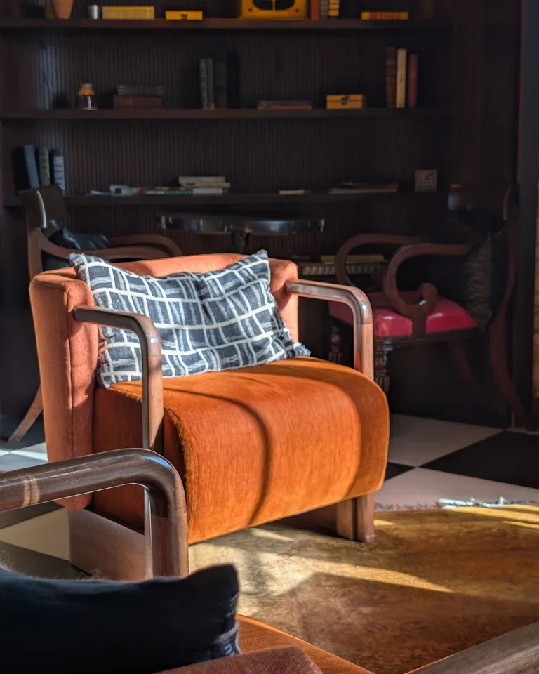 Rust-orange velvet accent chair with a patterned pillow in a living room