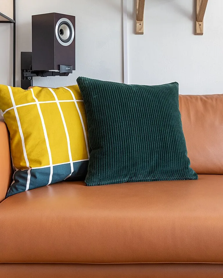 Decorative throw pillows in mustard yellow and deep green on a rust-orange leather sofa
