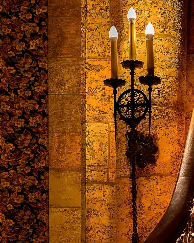 Candle-style wall sconce glowing against a textured plaster wall
