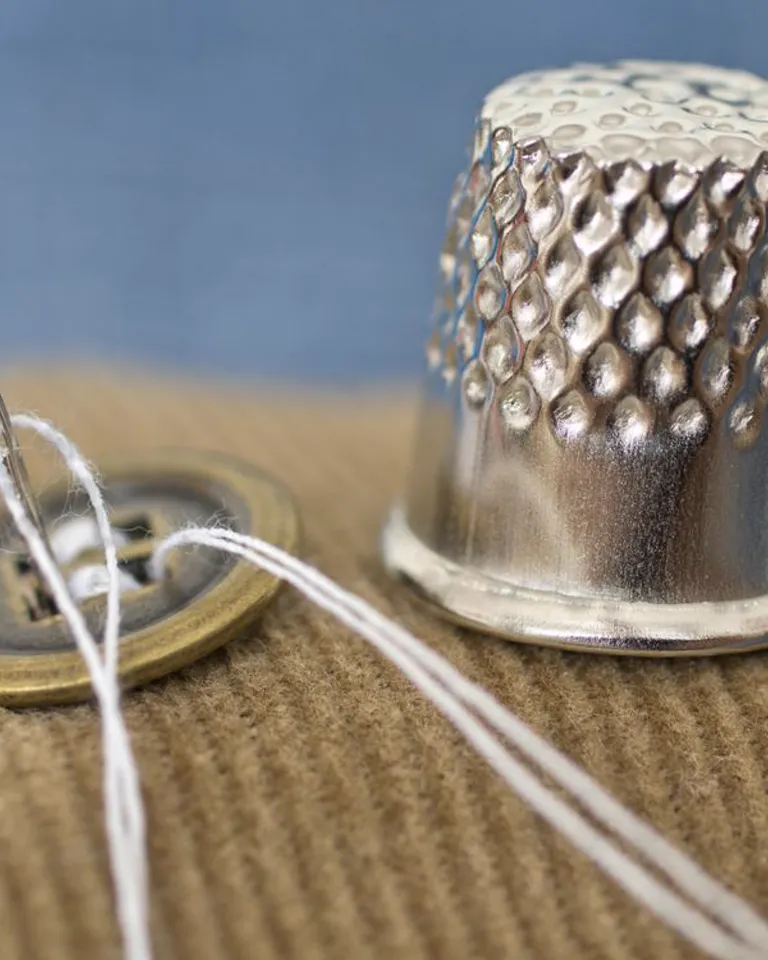 A silver sewing thimble beside a button and thread
