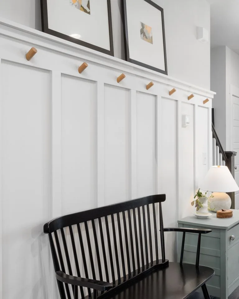 Wall-mounted peg hooks and a slim chest beside a doorway