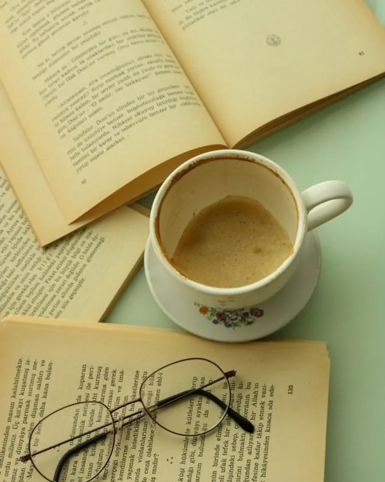 An open book, a cup of coffee and glasses on a table