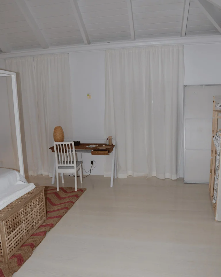 A minimalist bedroom with sheer curtains, a woven basket, and a small rug by the window