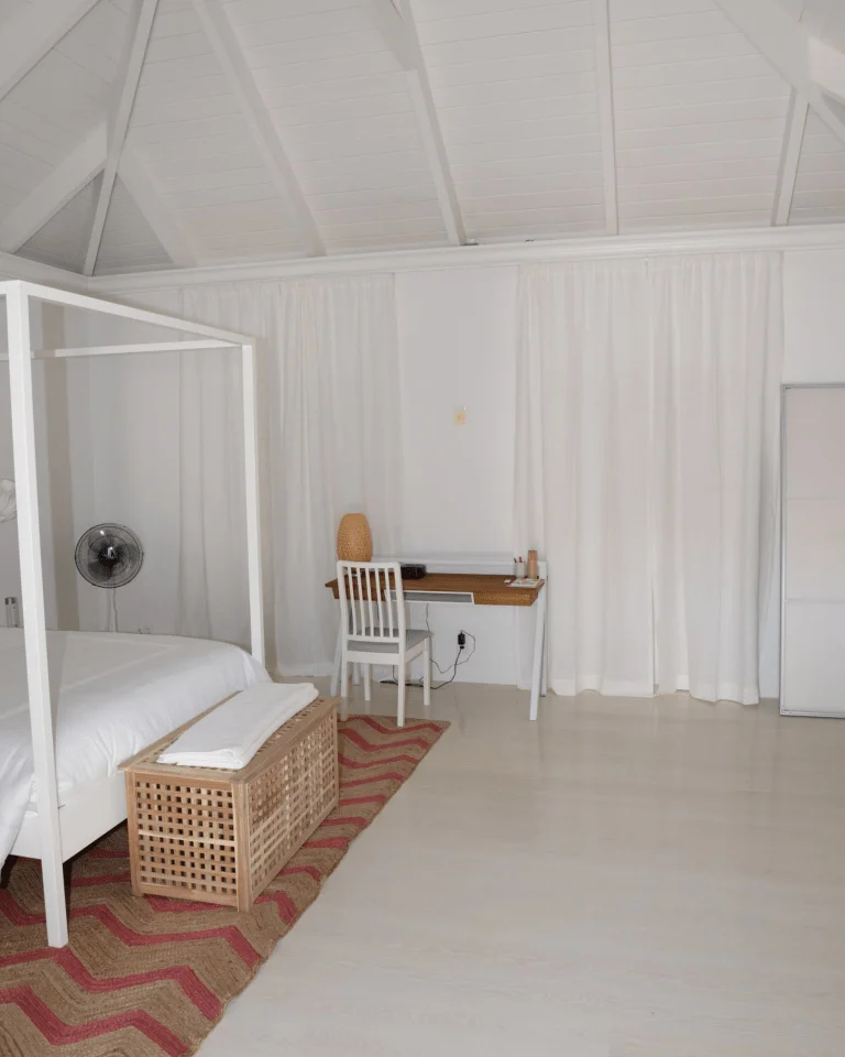 A bright bedroom with a woven rug under a four-poster bed, defining the sleeping area