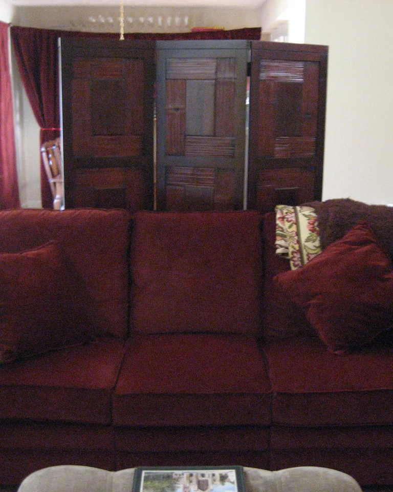 A wooden folding screen standing behind a sofa, dividing a living space