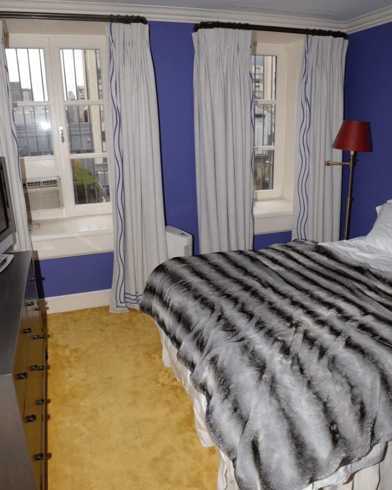 A bedroom with white curtains framing two windows beside a bed