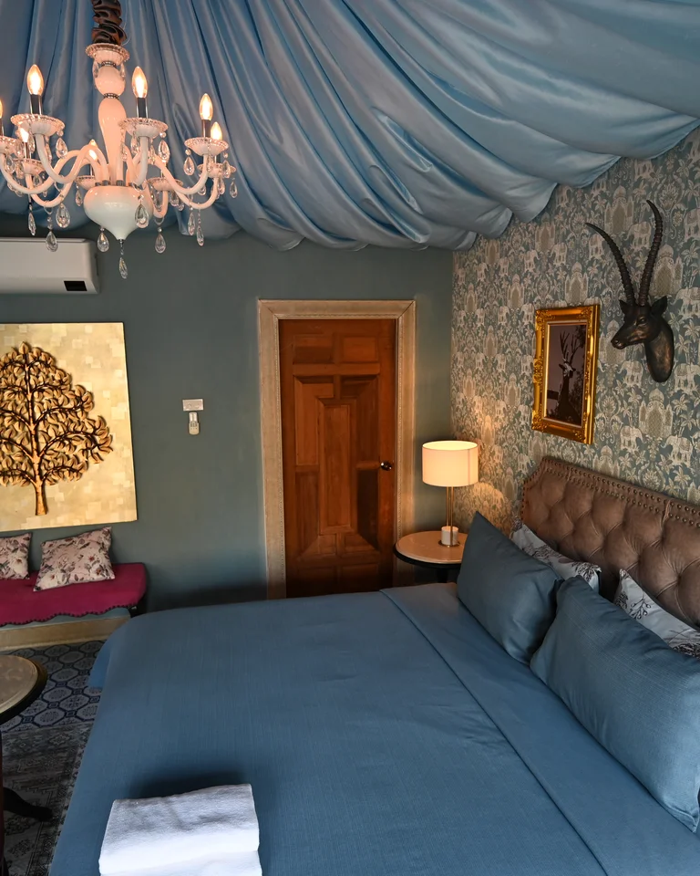 A bedroom with a tufted upholstered headboard, soft blue linens, and framed artwork