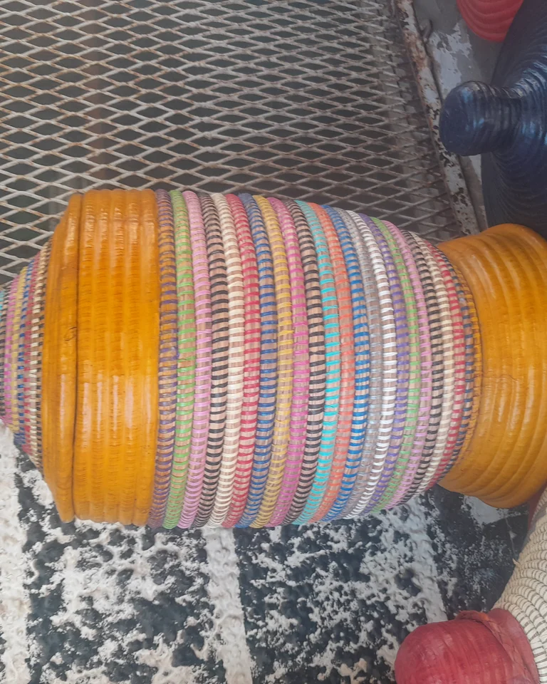 A woven laundry basket with a lid, made by artisans, standing against a wall