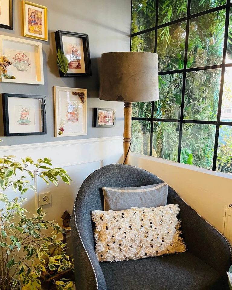 A reading chair with a floor lamp and framed art beside a large window