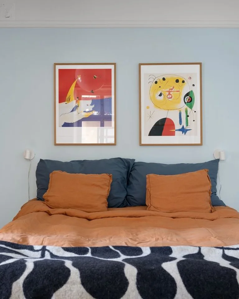 A bedroom in soft blue and warm orange showing one palette repeated in bedding and wall art