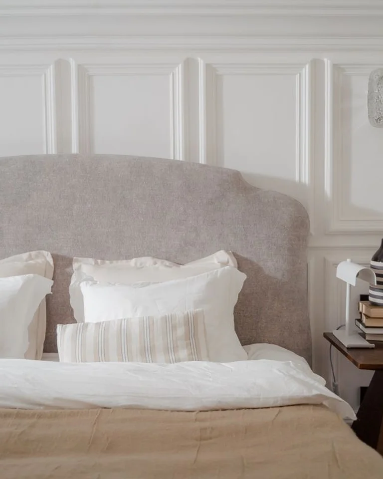 A bed with a grey upholstered headboard against a panelled wall with a bedside table and lamp