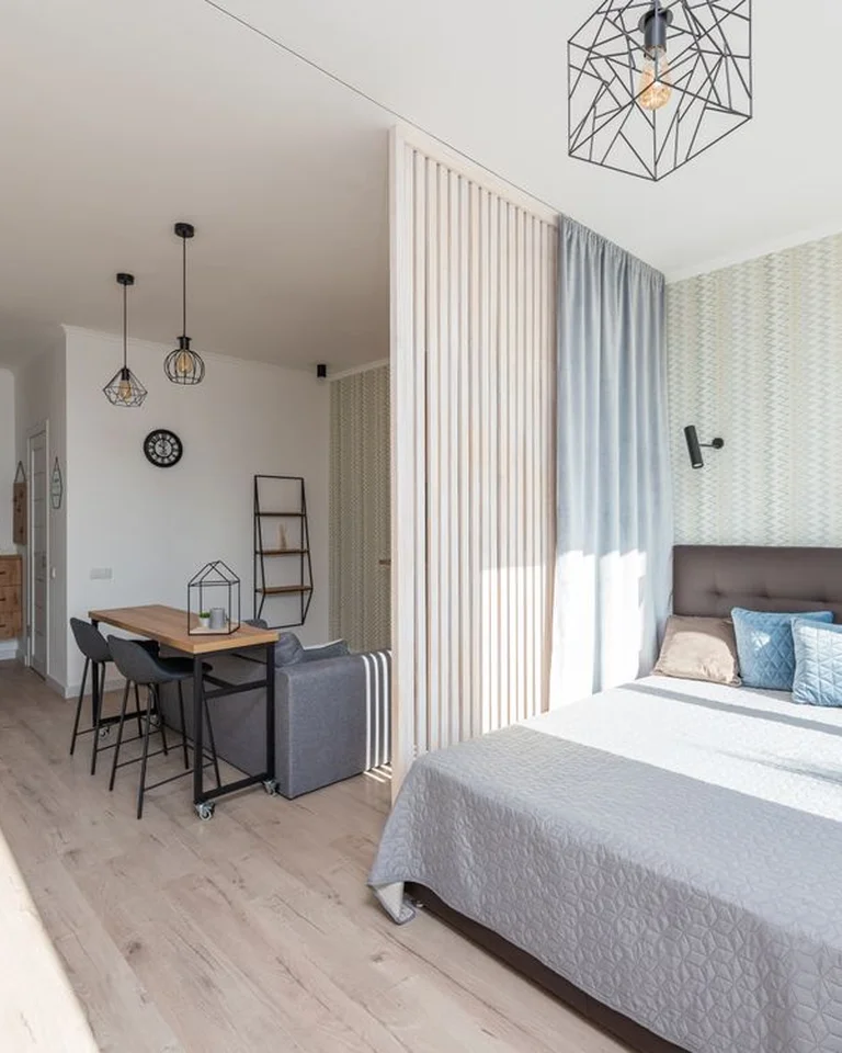 A bright studio apartment with a bed area separated from the living and dining space by a slatted divider