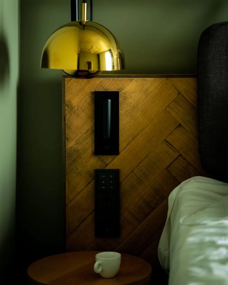 A cozy bed tucked into a corner with a wooden headboard panel and a small round side table