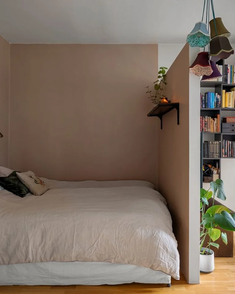 A tall open bookshelf used as a room divider beside a bed in a small apartment