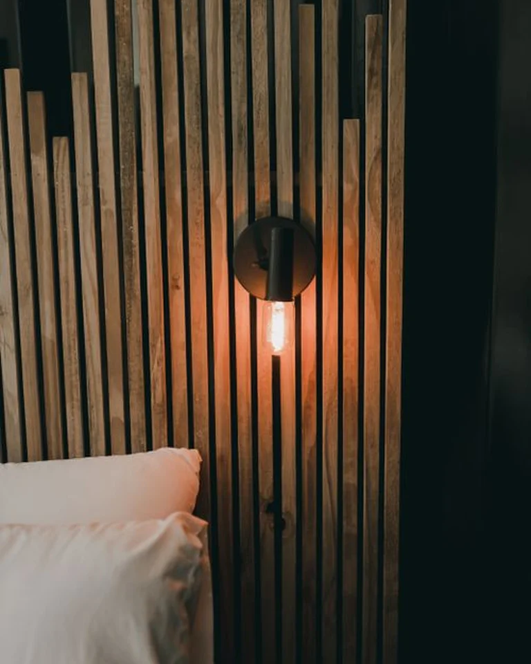 A bedroom wall finished with warm vertical wood slat panels behind the bed