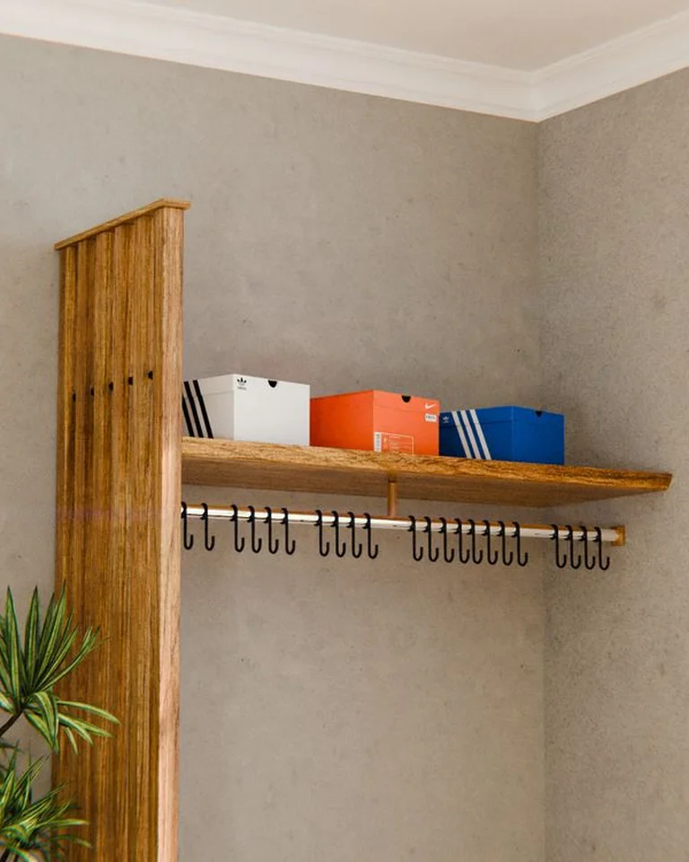 A small bedroom dressing corner with a mirror, wall hooks, and a stool