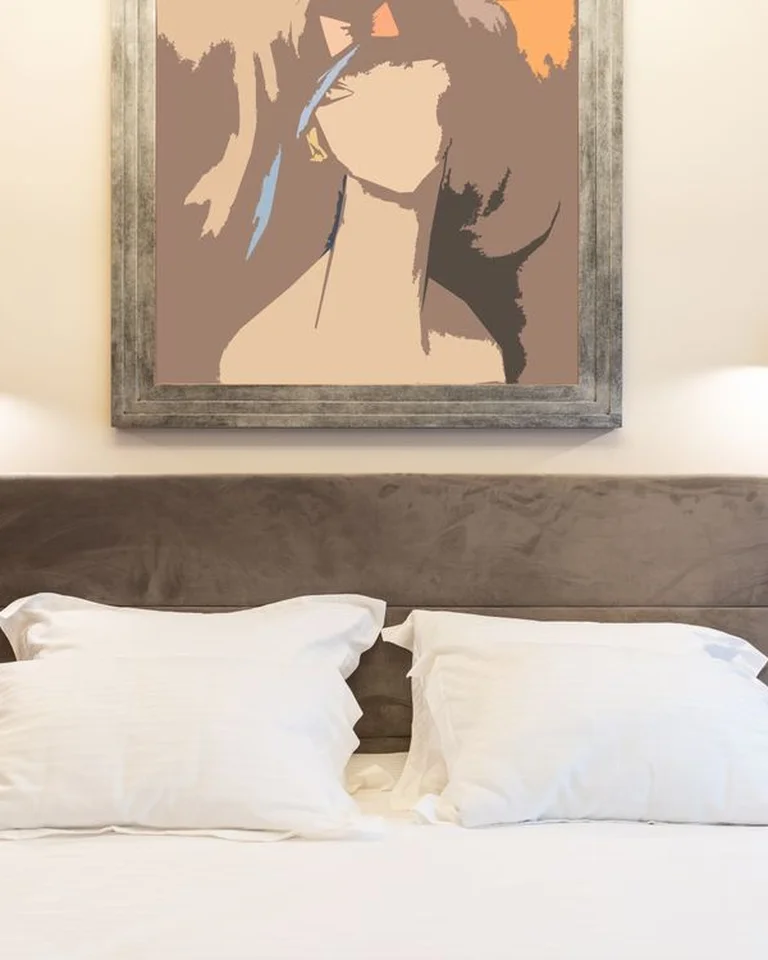A large framed artwork hanging above a bed with wall lights on either side