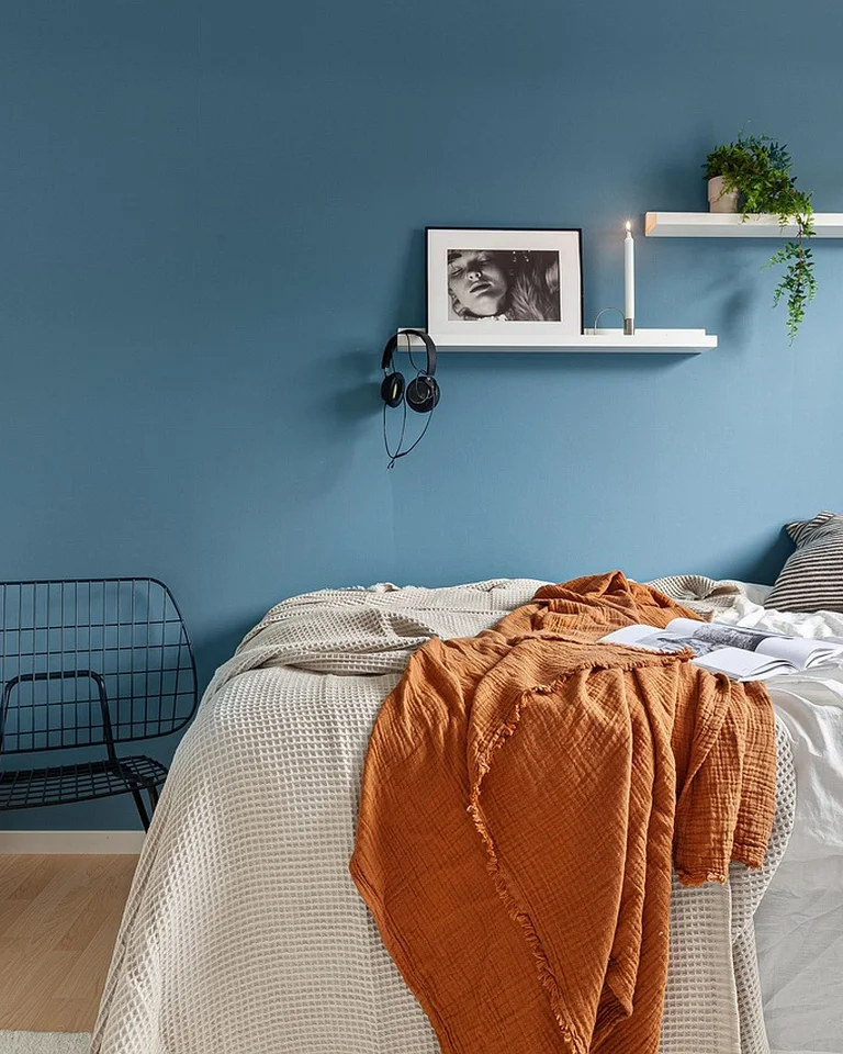 Shelves mounted on the wall above and around a bed in a small bedroom