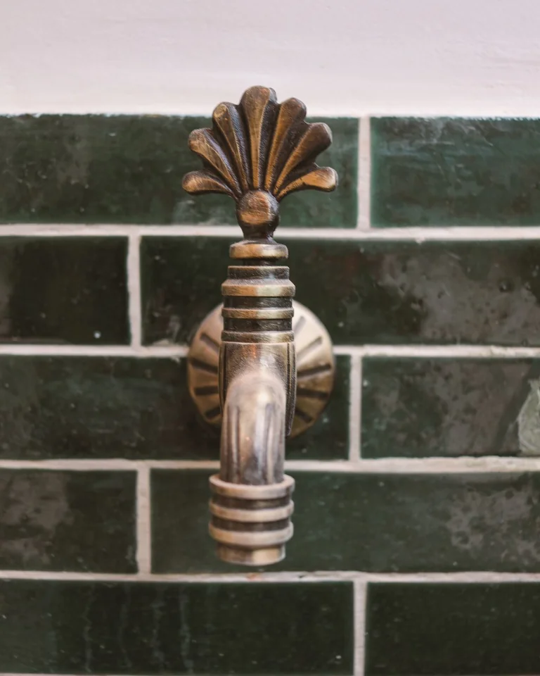 Close-up of brushed brass faucet against deep green bathroom tiles