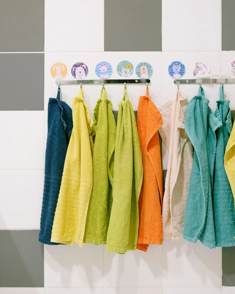 Colorful bath towels including green ones hanging on hooks in a bathroom