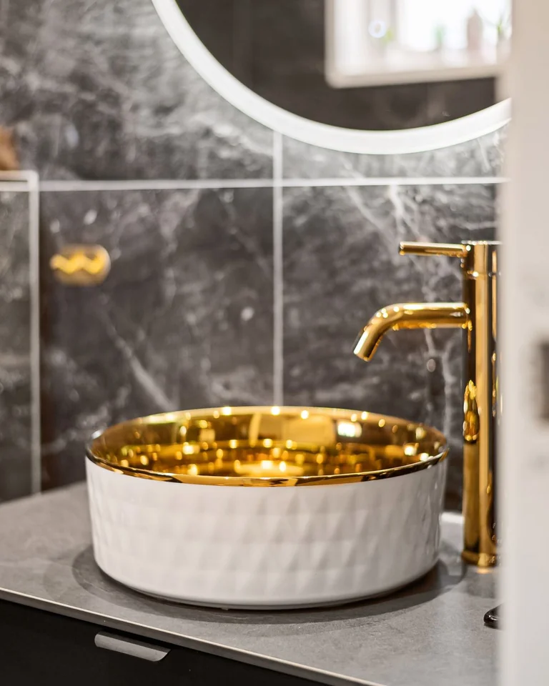 Close-up of a gold bathroom faucet with a gold-rimmed vessel sink