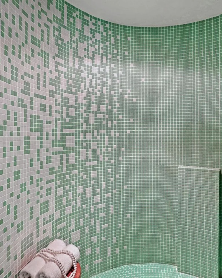 Curved shower lined with green and white mosaic tile