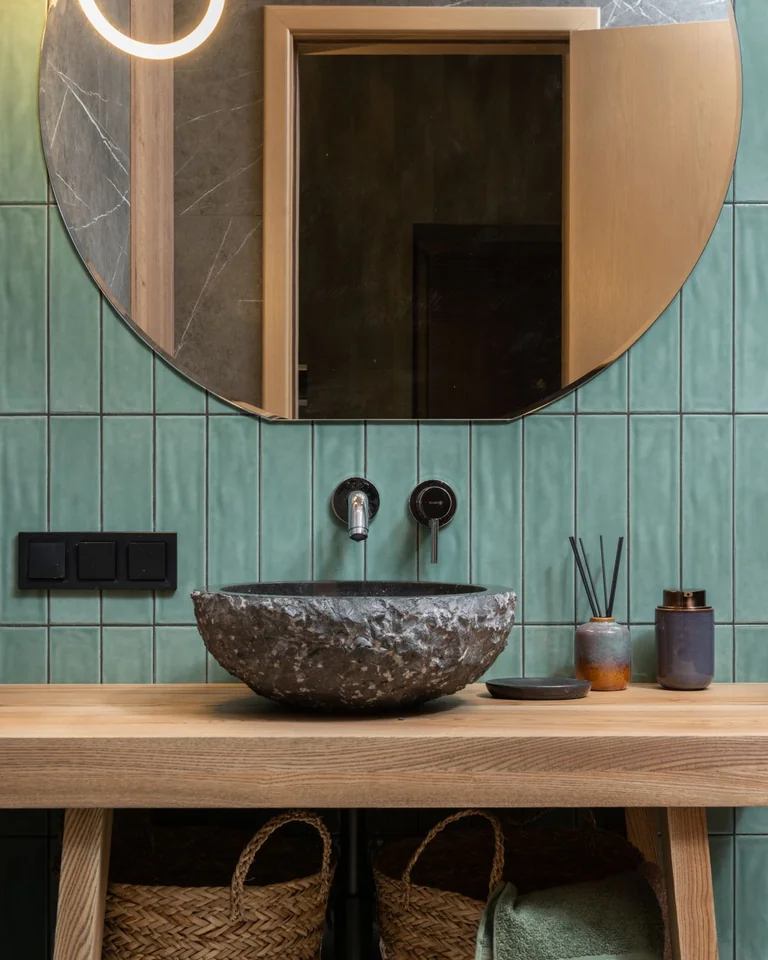 Small green bathroom with an oversized round mirror reflecting light