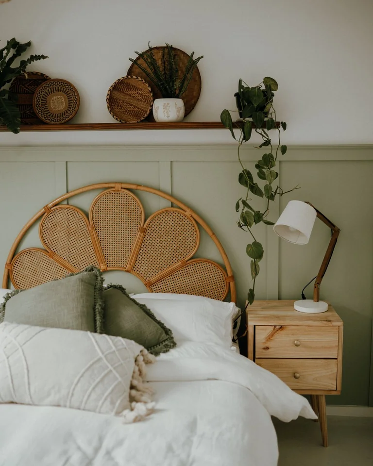 White bedding with sage green pillows on a bed against a sage paneled wall