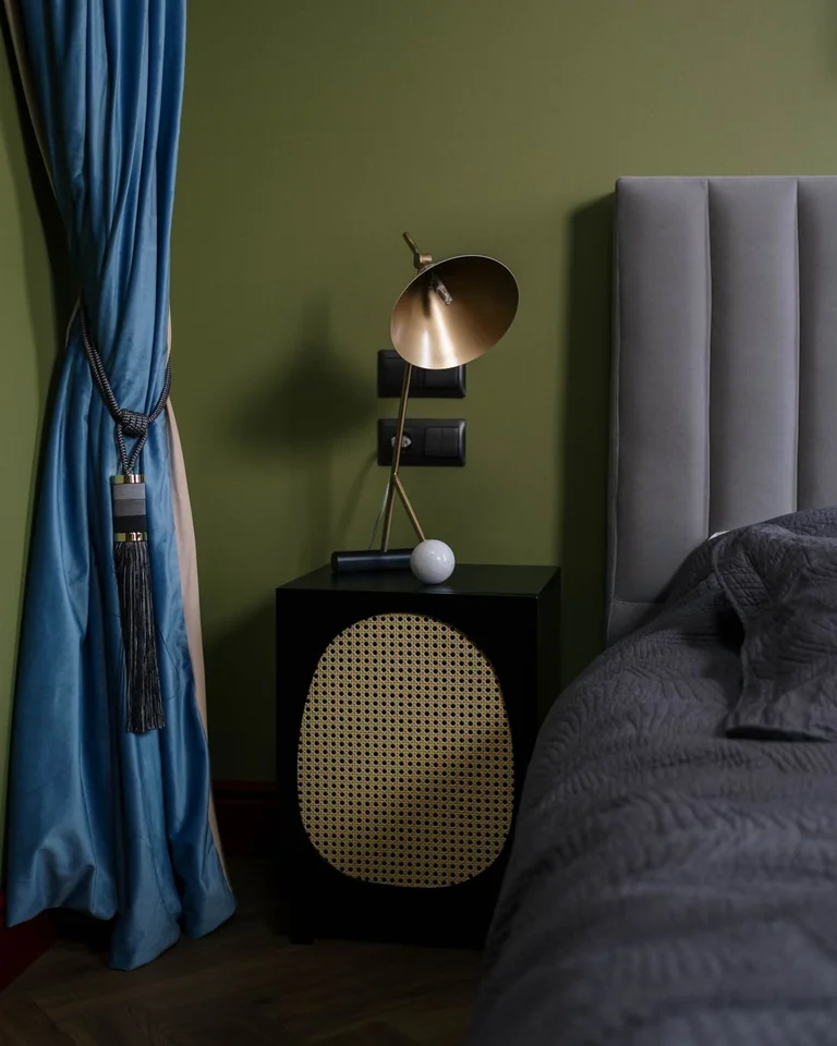 Brass table lamp on a nightstand against a deep green bedroom wall
