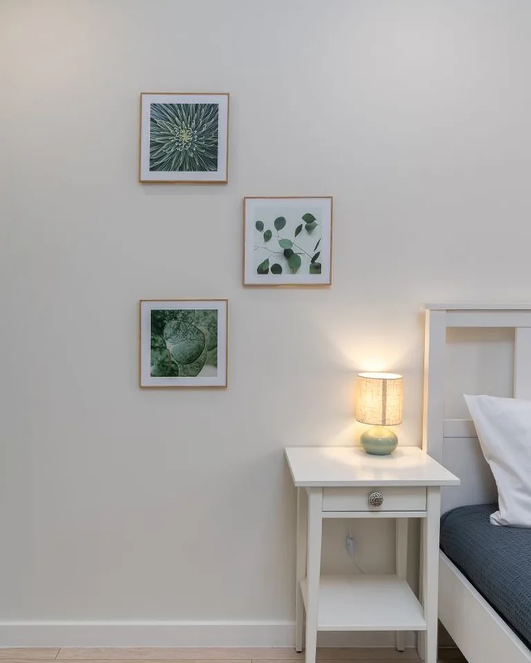 Three framed botanical prints on a bedroom wall above a white nightstand