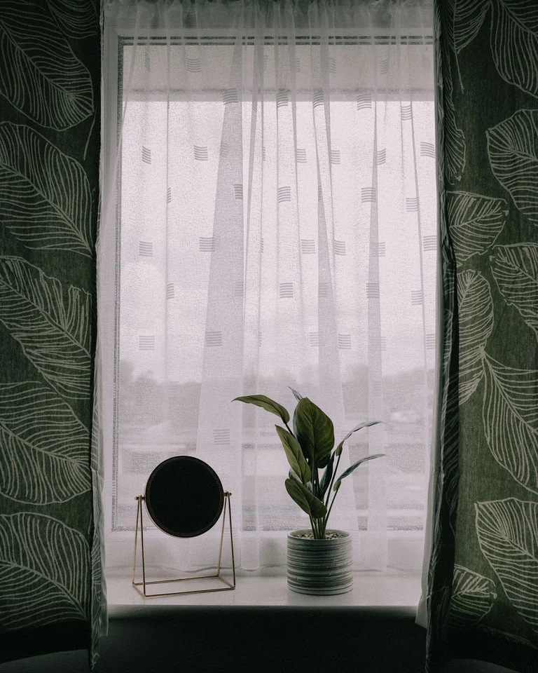 Window framed by dark green leaf-patterned curtains with a sheer white inner curtain