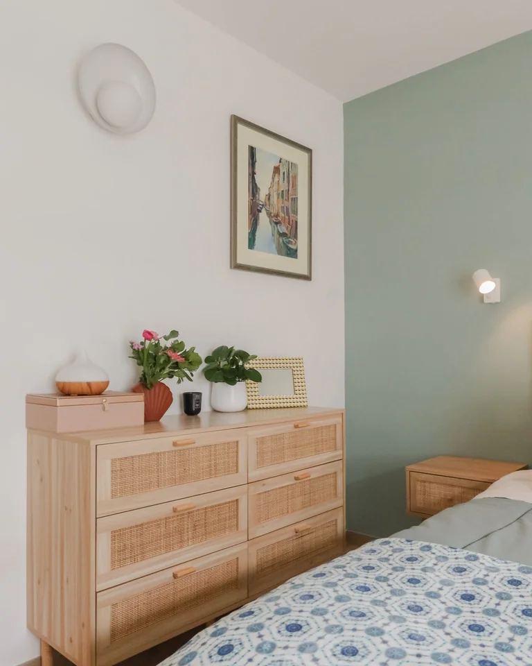 Wooden rattan-front dresser styled with plants and decor against a sage green bedroom wall