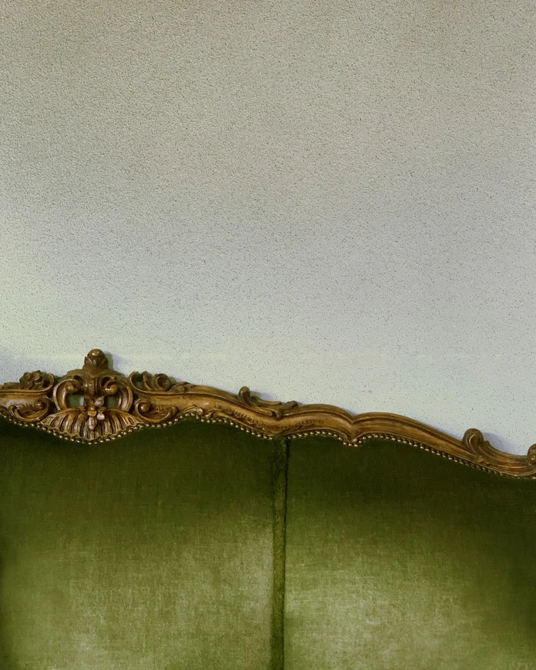 Bedroom with a sage green velvet upholstered headboard and brass lamps