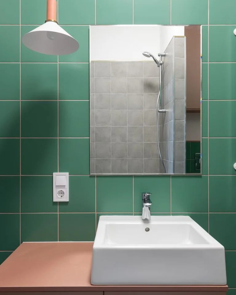 Small bathroom with green tiled walls and white sink and fixtures