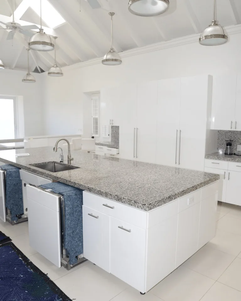 Bright white kitchen with granite island and pendant lights under skylights