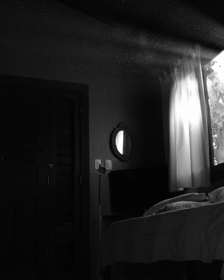 Bed by a bright window in a black and white bedroom