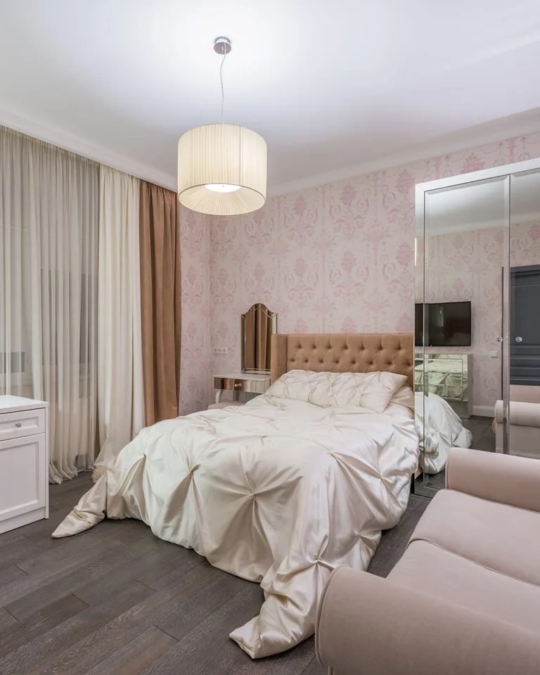 Bedroom with pink walls and furniture, large bed beside a table and chair