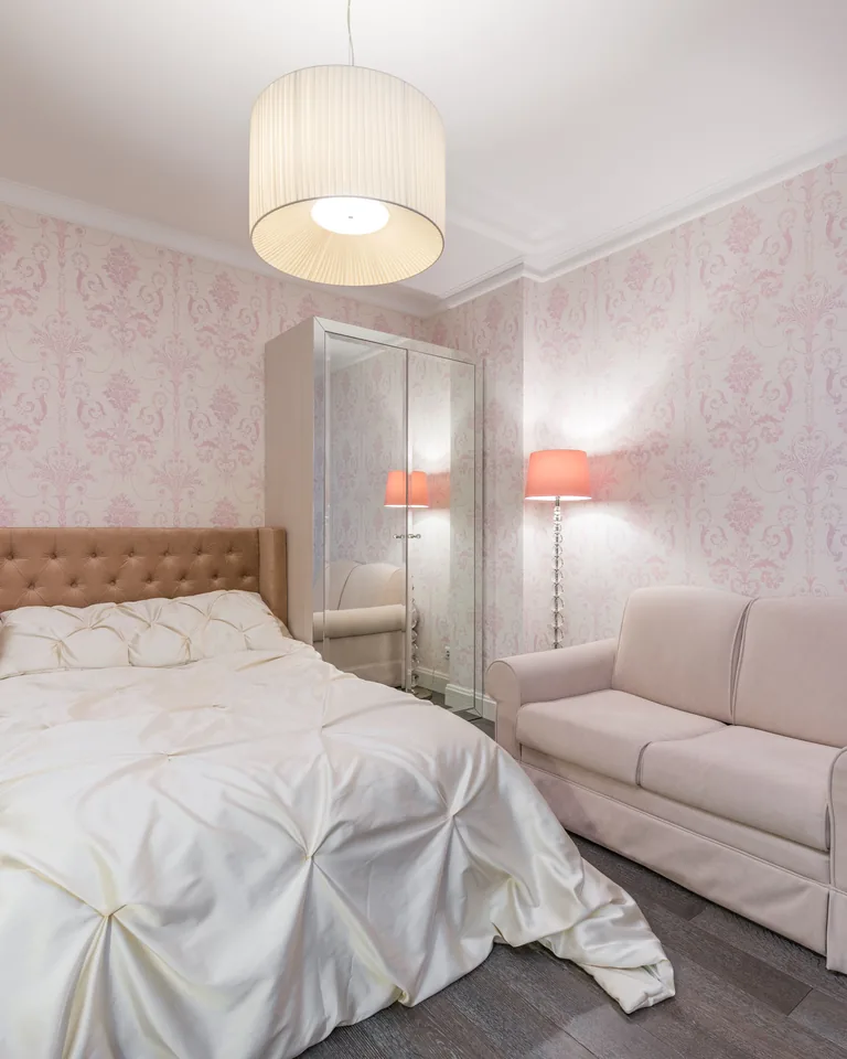 Large bed with white linen in a spacious bedroom with pink furniture and walls