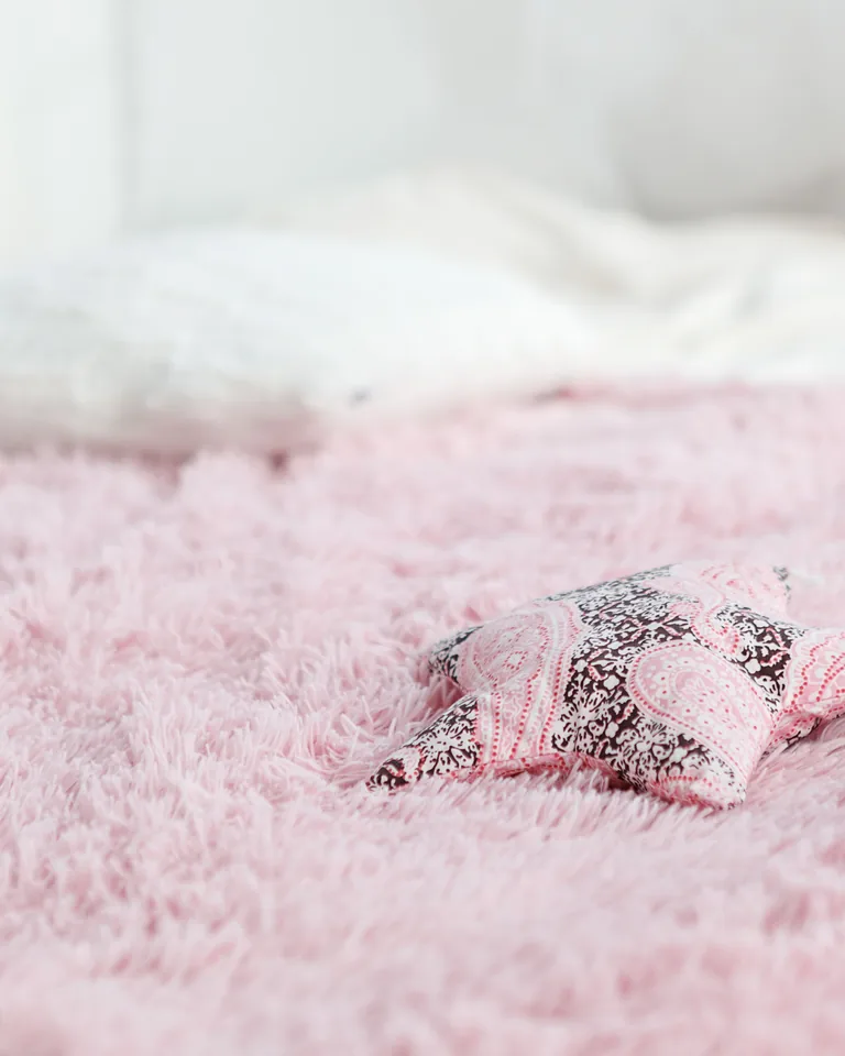 Soft pink fuzzy throw blanket with a decorative star pillow on a bed