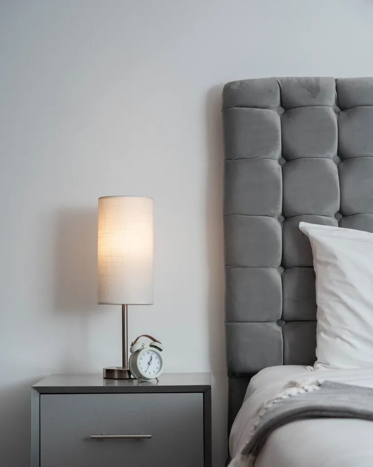 Bedroom with a grey upholstered headboard, bedside lamp and nightstand